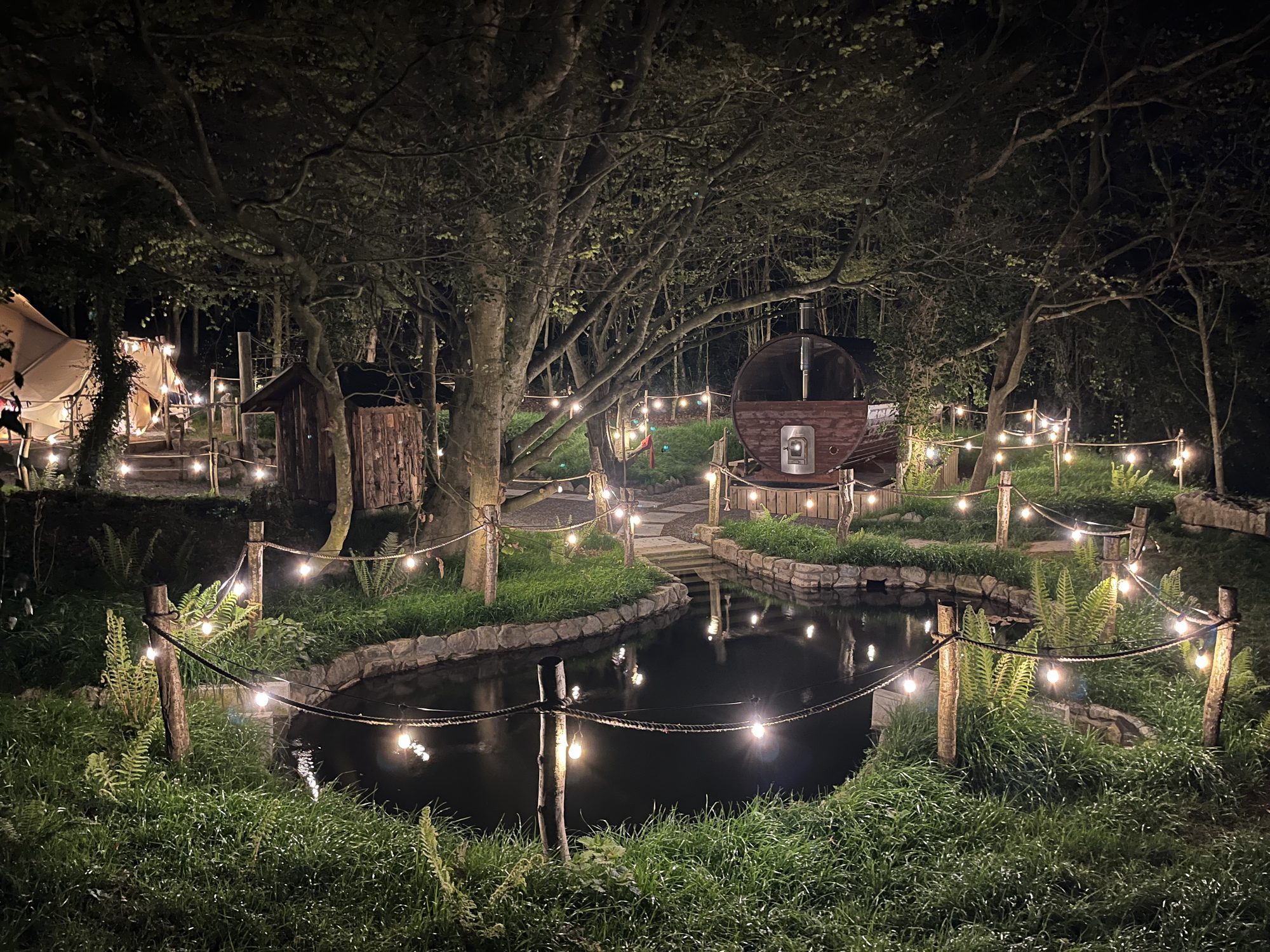 The spring-fed plunge, sauna and changing yurt lit by festoon lights at night