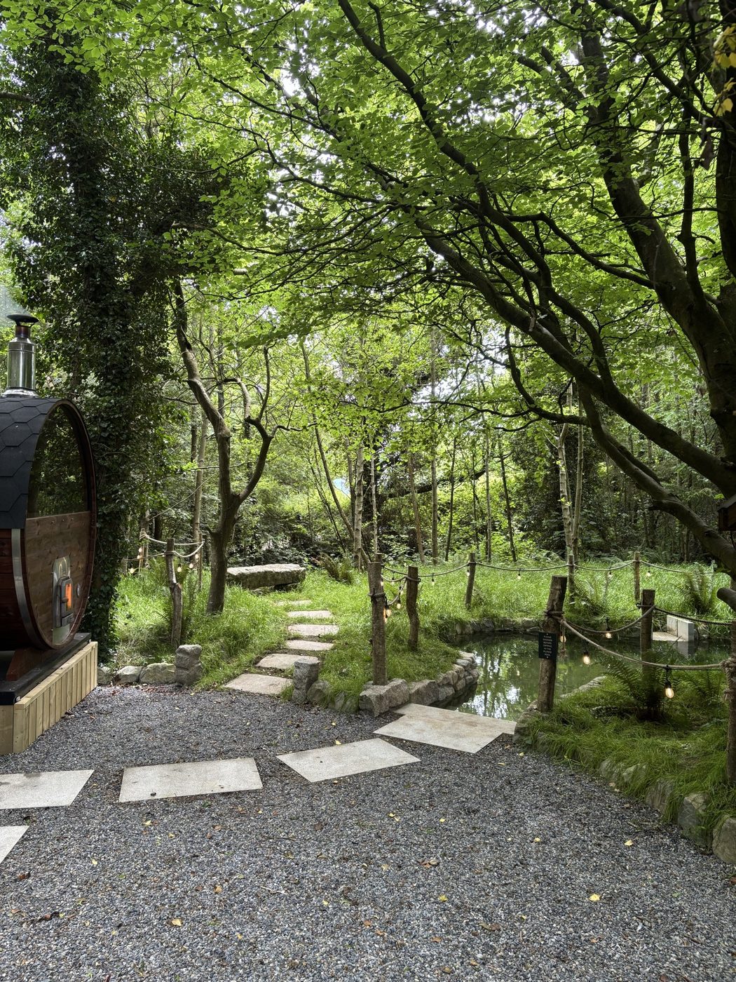 Granite paving and gathered stone edging the spring-fed plunge beside the barrel sauna