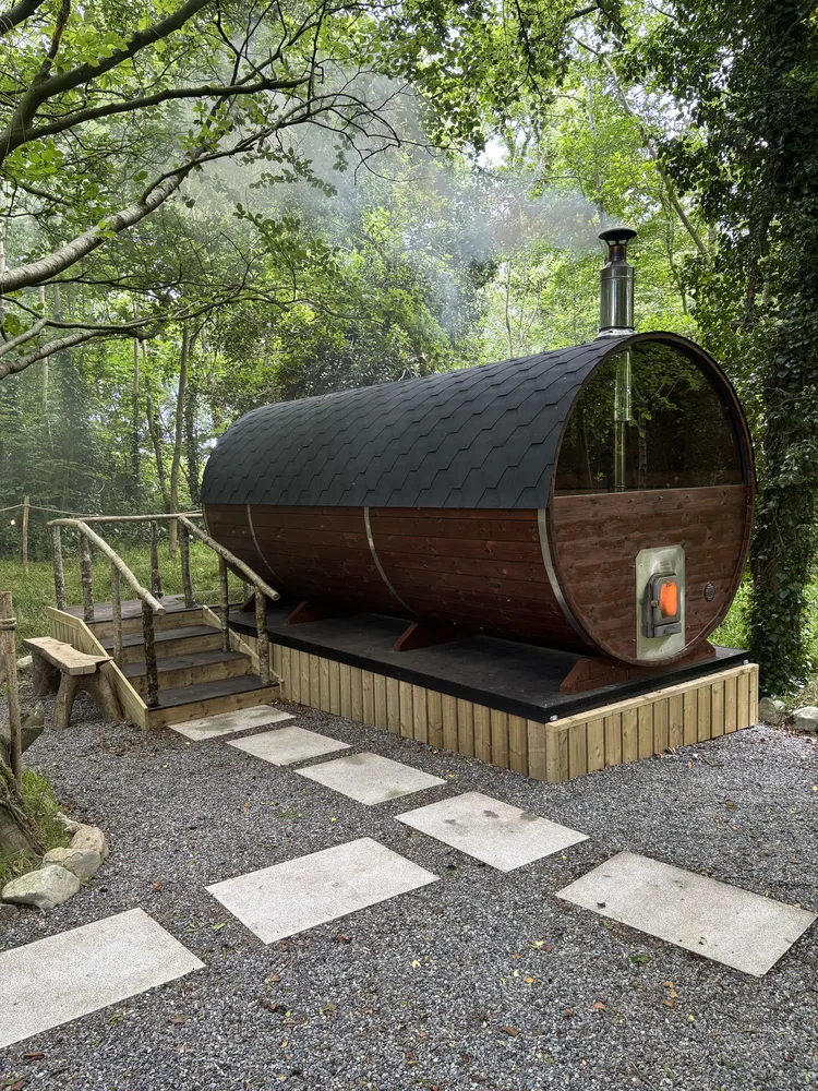 The barrel sauna among the trees, steam rising into the evening air